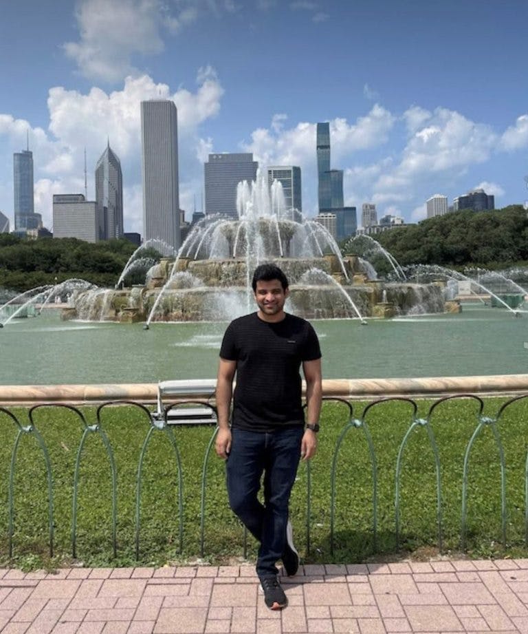 Anish Pahwa standing in front of a fountain with a downtown cityscape in the background.
