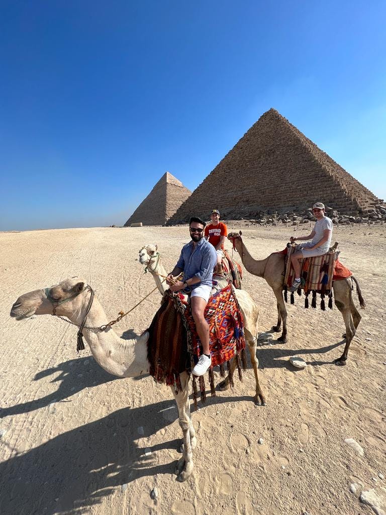 Photo of Alvaro Luna riding a camel in the desert near pyramids in Egypt